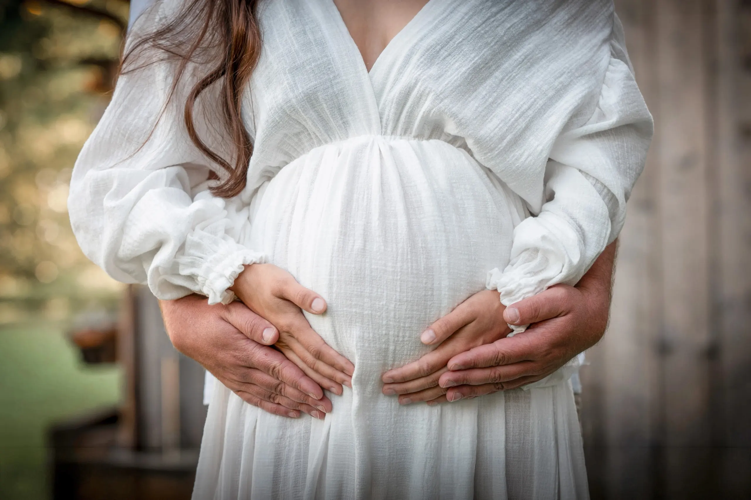 Zwei Händepaare liegen gemeinsam auf einem Schwangerschaftsbauch
