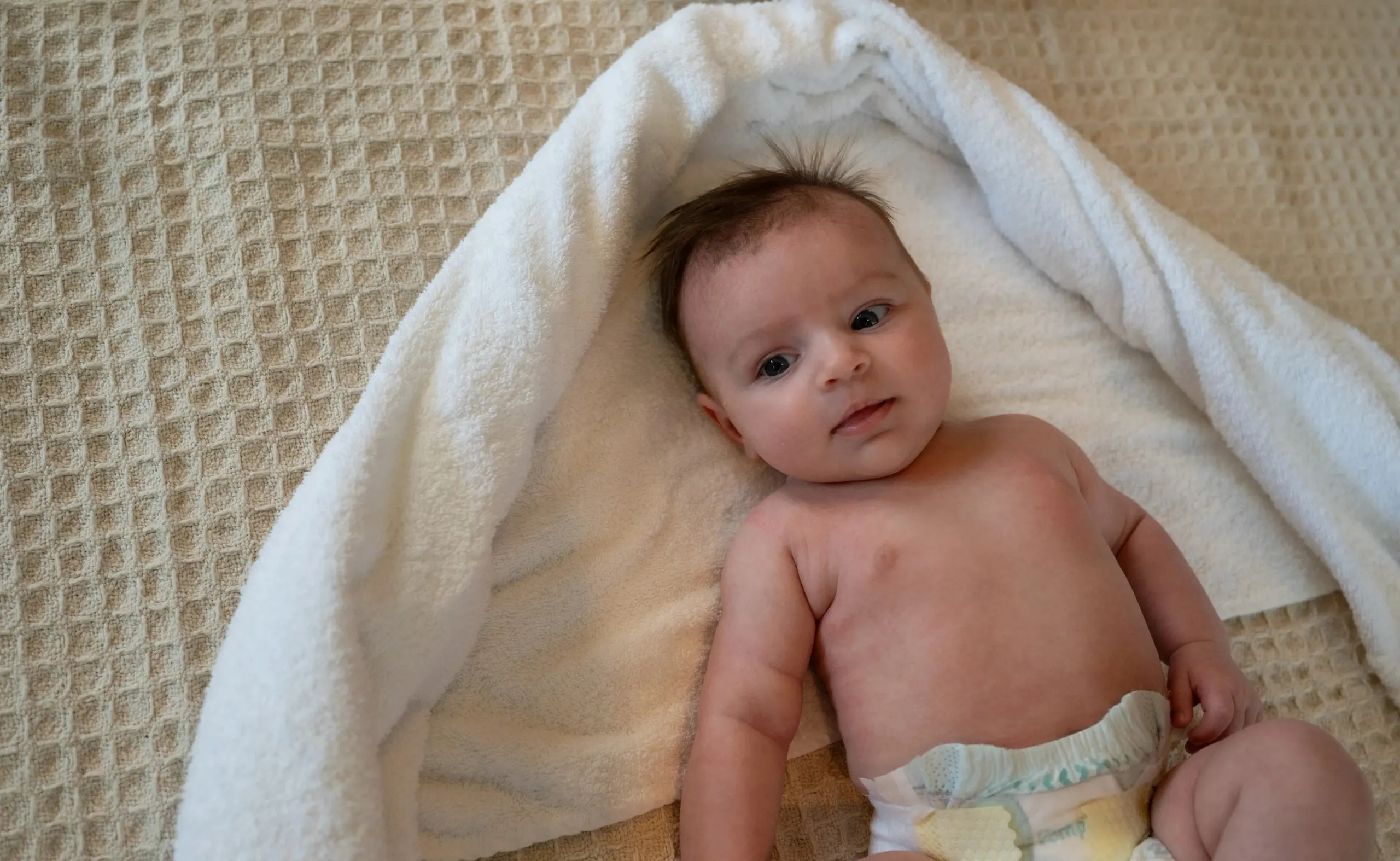 Baby liegt in ein weiches weisses Tuch gehüllt und schaut in die Kamera
