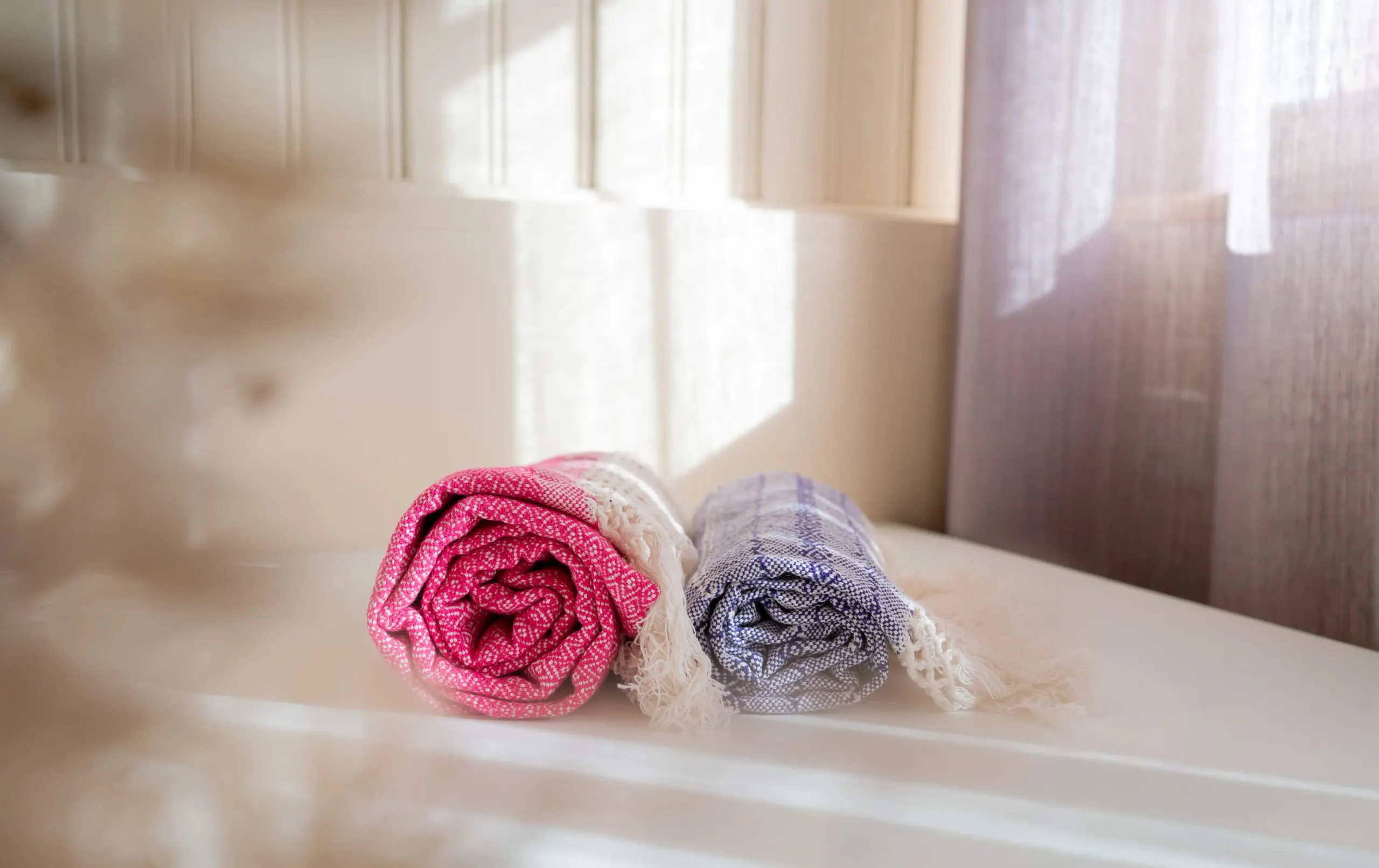 Zwei zusammengerollte Rebozo-Tücher in Rosa und Flieder auf einer sonnigen Fensterbank