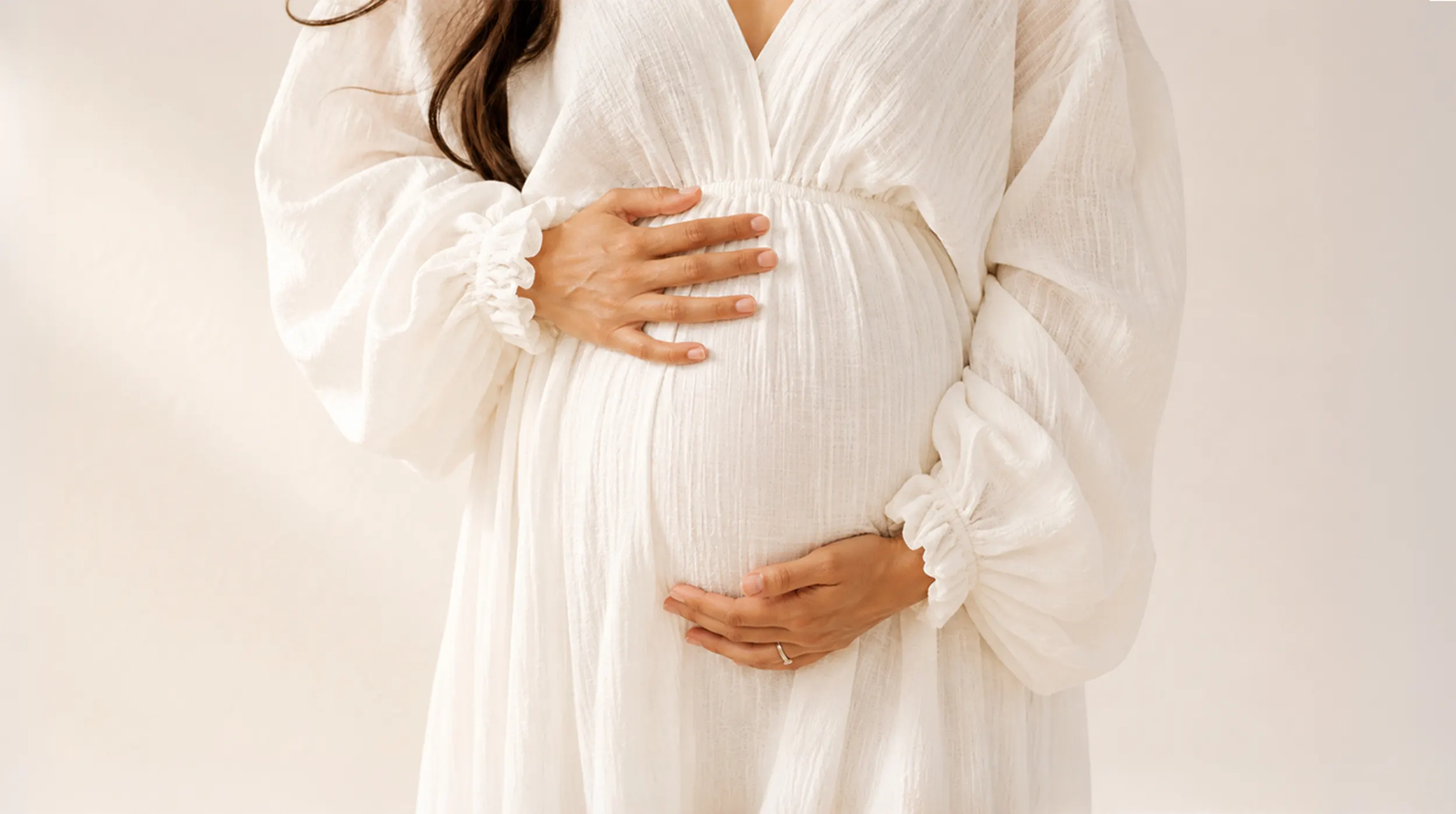 Schwangere Frau in einem weissen Kleid, die ihren Bauch mit beiden Händen hält